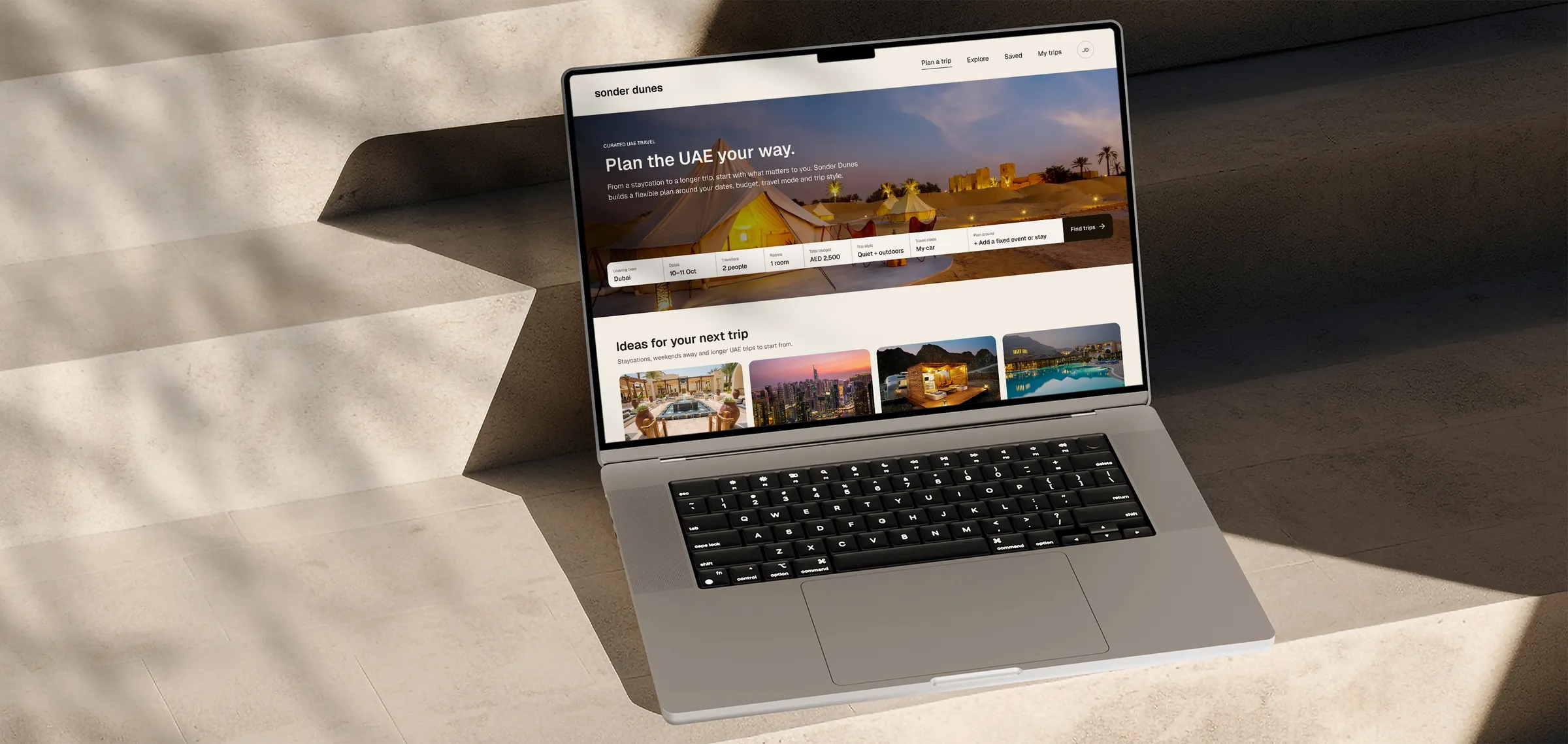 The Sonder Dunes trip planner on a laptop, resting on stone blocks.